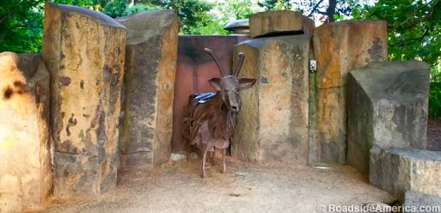 Brown goat made of metal stands in a rocky grotto.
