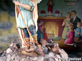 Angel spears Devil while a family prays to fireplace Jesus.